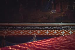 a bed with a red bedspread and a painting on the wall — Photo Czapp Botond / Unsplash