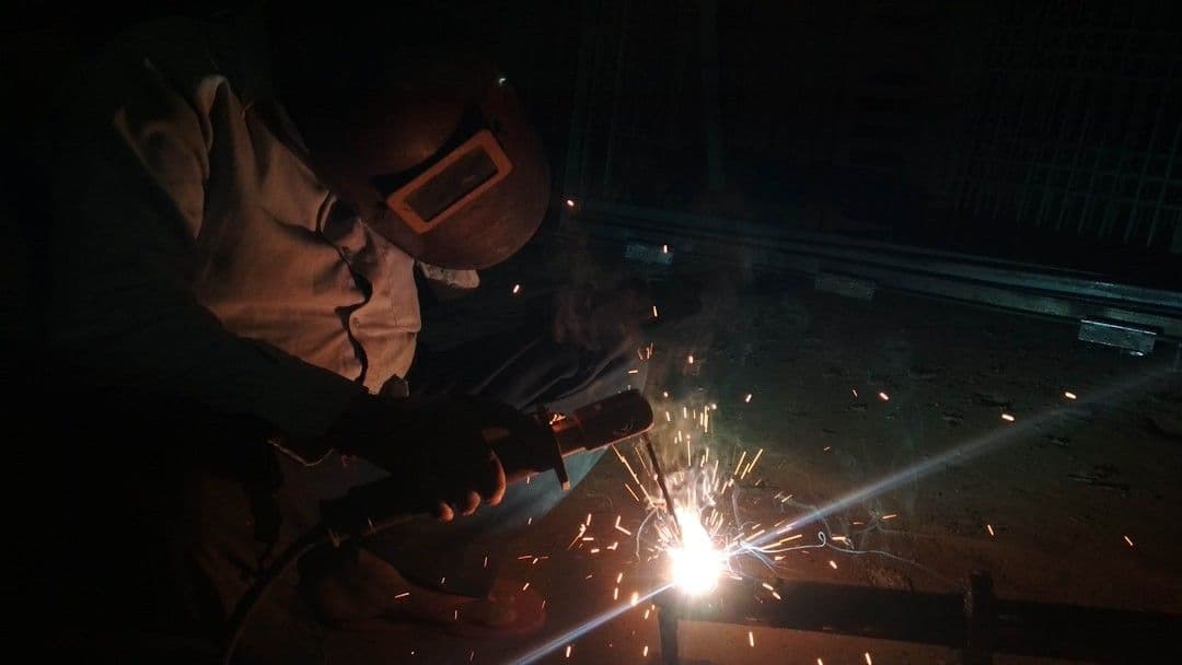 a man welding a piece of metal in the dark — Photo Surya Prakash / Unsplash