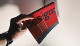 Tattooed hand holding a red book about design. — Photo @felirbe / Unsplash