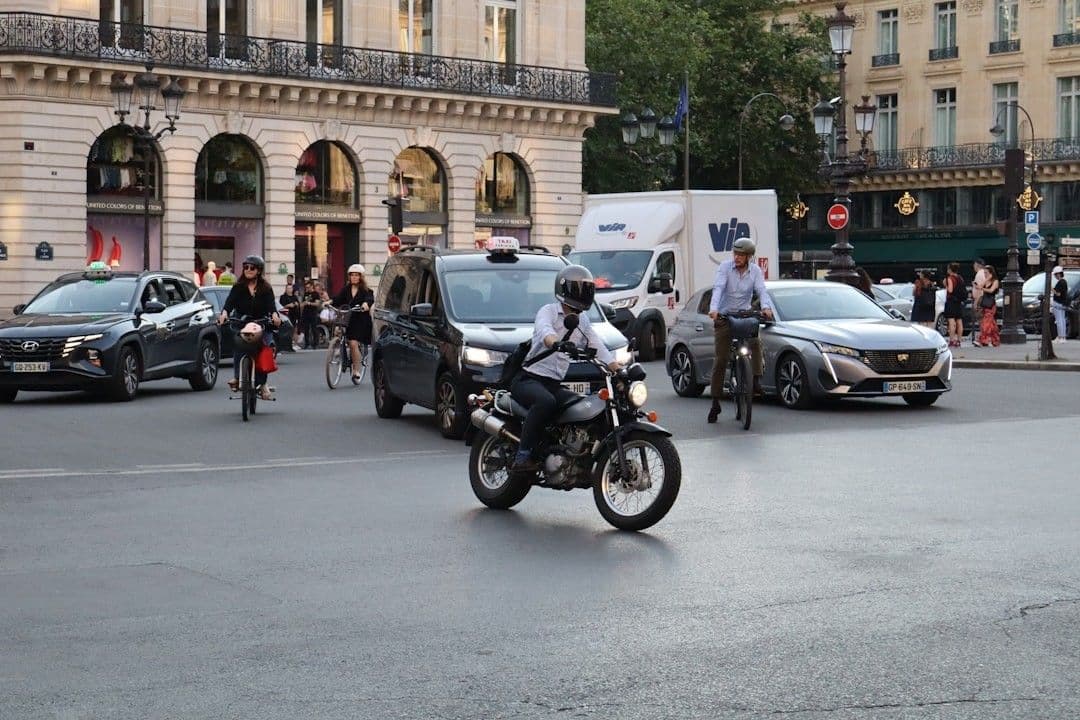 A man riding a motorcycle down a street next to tall buildings — Photo Ethan / Unsplash