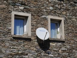 A satellite dish mounted to the side of a stone building — Photo jens schwan / Unsplash