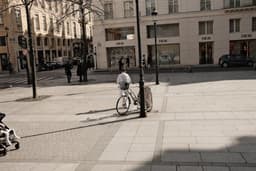 a man riding a bike down a street next to tall buildings — Photo Valentin Lacoste / Unsplash