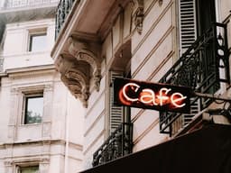 a cafe sign is lit up outside of a building — Photo Mathias Reding / Unsplash