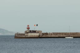 Lighthouse on a stone pier with a sailboat. — Photo Jonathan Borba / Unsplash