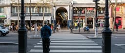 a man standing at a crosswalk in the middle of a city — Photo Valentin Lacoste / Unsplash