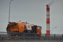 An orange truck passes a smokestack. — Photo Konstantin Kitsenuik / Unsplash