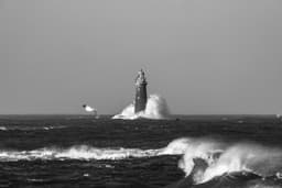 a black and white photo of a lighthouse in the ocean — Photo Osman Rana / Unsplash