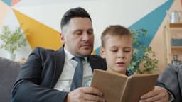 Man in suit and little kid are reading book in cozy apartment concentrated on education, businessman is spending leisure time with son. Family and hobby concept. — Photo Vitaly Gariev / Unsplash