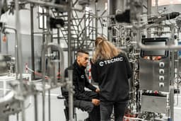 Two people checking a stainless steel bioreactor with integrated control screen in a technical validation and testing environment. — Photo TECNIC Bioprocess Solutions / Unsplash