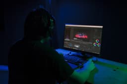 a man sitting in front of a computer in a dark room — Photo Tom Caillarec / Unsplash